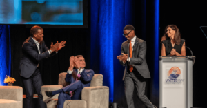 Fall Event speakers John Hope Bryant, Christopher Gorman, Mayor Justin Bibb, and Sharon Sobol Jordan onstage, smiling and clapping.