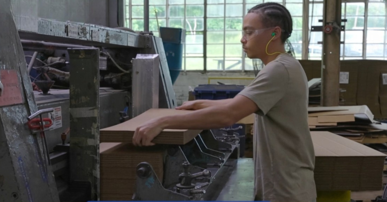 young man working at a machine folding boxes